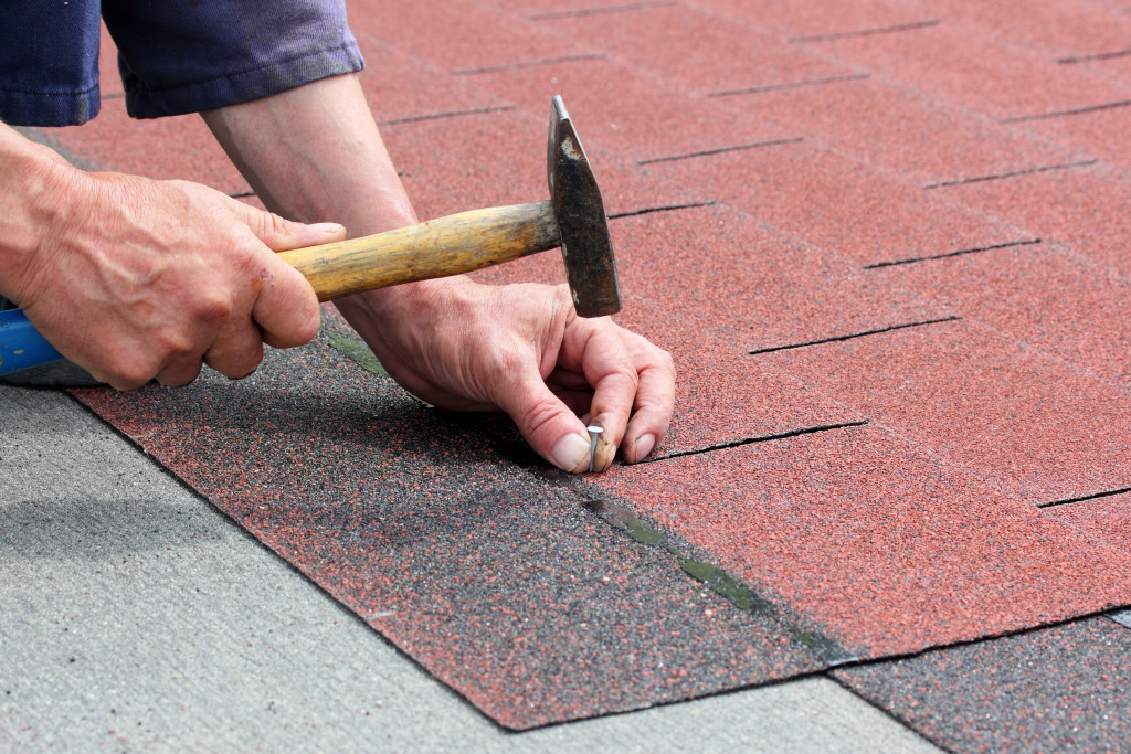 A builder hammering nails to install roof asphalt shingles