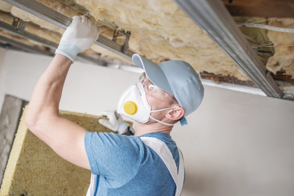 A worker installing wool insulation on the ceiling