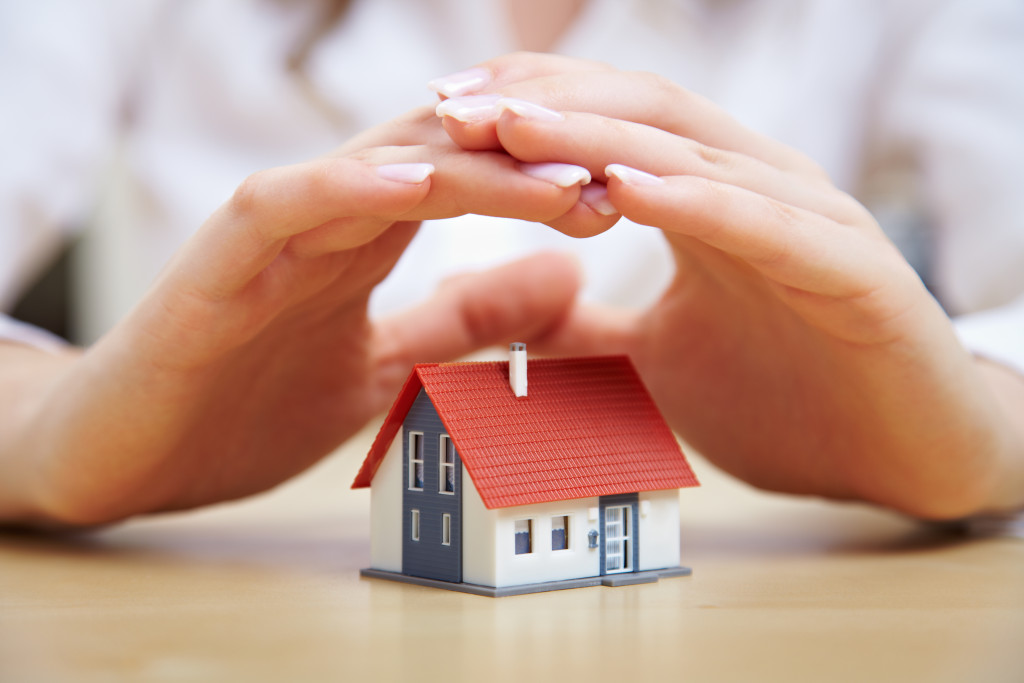 person's hands covering a house as if protecting it