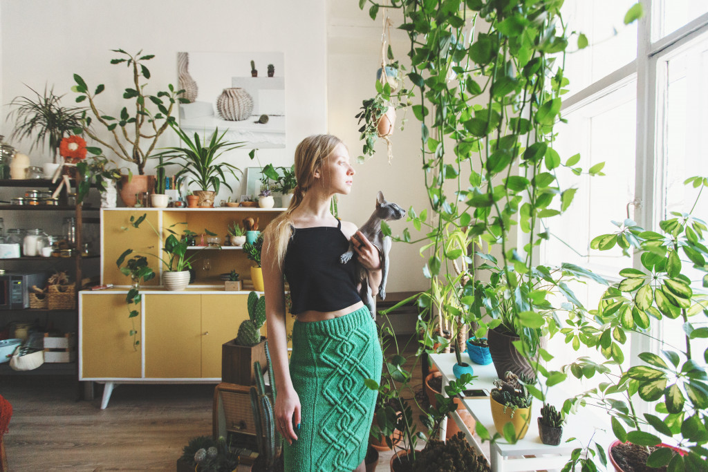 Young woman holding her cat inside a home with several indoor plants.