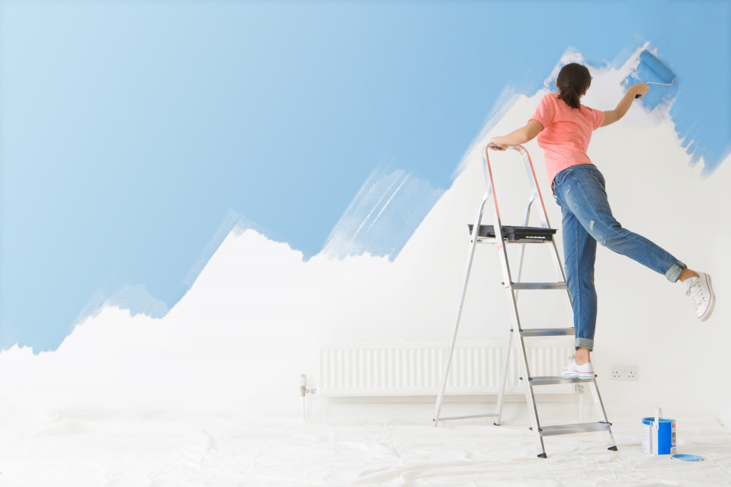 Young woman painting the interior wall of a house while standing on a ladder.