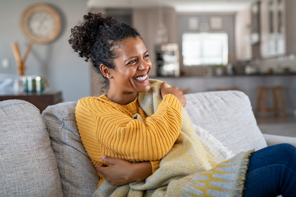 woman with curly hair smiling while cuddling a blanket in the living room