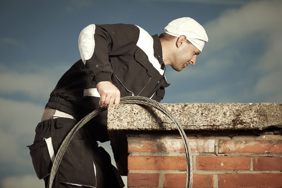 A man on the roof cleaning a brick chimney